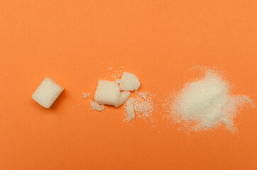 Top view of whole sugar cubes, crashed one and heap of sugar on the orange background