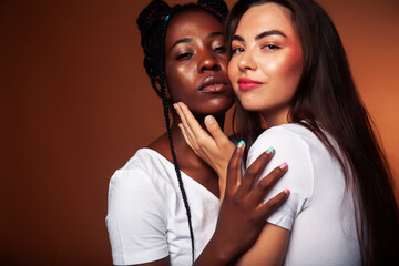 young pretty caucasian, afro woman posing cheerful together on brown background, lifestyle diverse nationality people concept