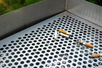 Cigarettes butts on grille of ashtray that stand in the smoking area.