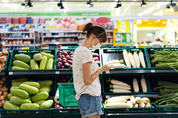 Young woman with face mask using mobile phone and buying groceries in the supermarket