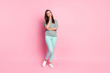 Fototapeta na wymiar Full size photo of thinkable sweet girl stand look empty space wear blue pants sneakers shirt isolated on pink color background