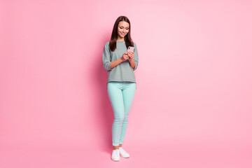 Full size photo of optimistic cute young woman stand write sms wear blue pants sneakers shirt isolated on pastel pink color background