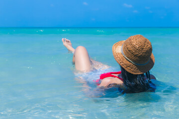 Beautiful woman in bikini on tropical beach. Portrait happy young asian woman enjoying at sea. Traveler woman in bikini and straw hat, sit on beach and feel relaxing. summer vacation time