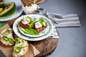 Sandwiches with soft cheese, avocado and cucumber. Breakfast is on the table. Healthy food. Toast and spread on it. Avocado sandwich stilllife. Healthy food. Toast. Copy space. Grey background.