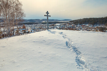 A path in the snow to the memorial cross installed on a mountain in a Russian Orthodox village