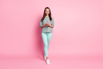 Fototapeta na wymiar Full size photo of optimistic nice young woman going look telephone wear blue jeans sneakers pullover isolated on pink background