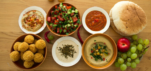 Traditional food of Israel on dark grey background with copy space. Colorful authentic meals top view photo: plate of hummus, falafels, salad, pita bread and tahini sauce. 