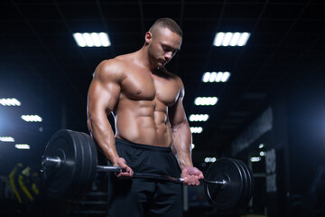 Fototapeta na wymiar Muscular sexy bodybuilder is working out doing weight lifting of the barbell in gym