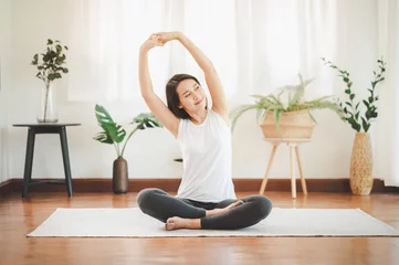 Fotobehang Glimlachende gezonde Aziatische vrouw die yoga schouder doet die zich thuis in de woonkamer uitstrekt © interstid
