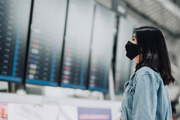 Fototapeta premium Asian woman traveler wearing mask protect from coronavirus looking flight information board display
