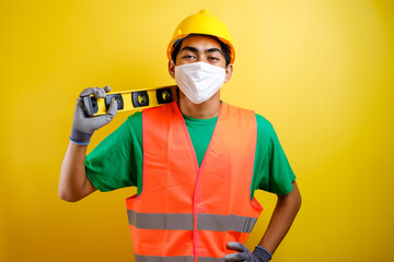 Asian constructor worker man with mask and safety vest hold waterpass on his shoulder
