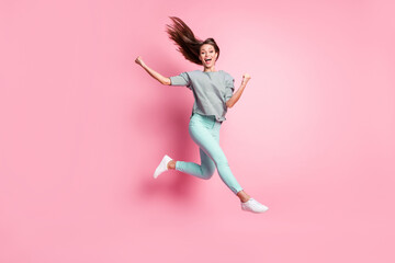 Full size photo of cheerful astonished girl jumping hands fists wear shirt pants sneakers isolated on pastel pink color background