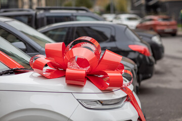 a white car with a big, red bow on the hood is on the street, an expensive gift, a new car as a gift, a gift car