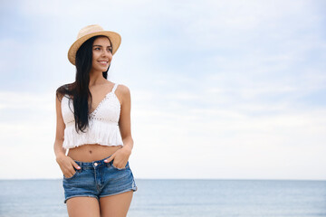 Fototapeta na wymiar Beautiful young woman with beach hat near sea. Space for text