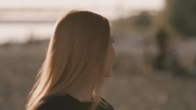 Face of young beautiful woman on the beach during amazing sunset who is turing left. She is smiling gently.