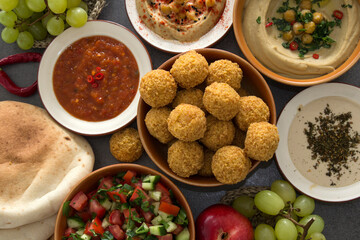 Traditional food of Israel on dark grey background with copy space. Colorful authentic meals top view photo: plate of hummus, falafels, salad, pita bread and tahini sauce. 