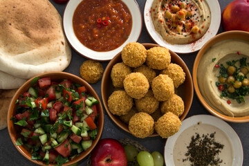Traditional food of Israel on dark grey background with copy space. Colorful authentic meals top view photo: plate of hummus, falafels, salad, pita bread and tahini sauce. 