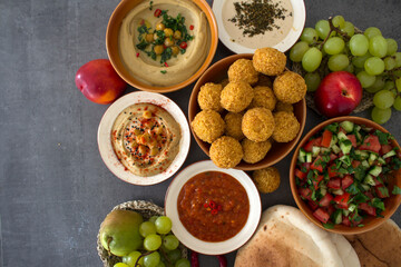   Authentic food of Middle East. Plate of hummus, falafels, pita bread, harissa sauce, tahini, fresh salad and fruits on wooden table. Traditional meals of Israel top view photo. Beautiful food pictur