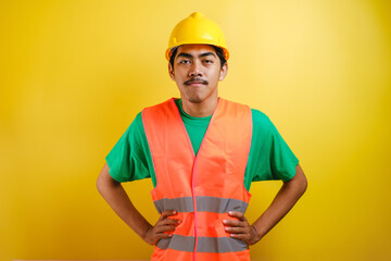 Asian construction worker smile looking to camera placing his both hand on his waist - obrazy, fototapety, plakaty