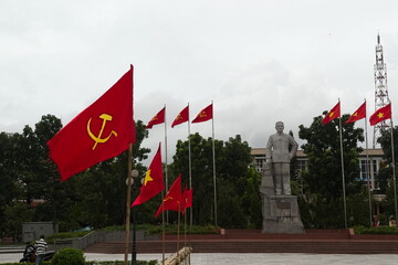 Dong Ha, Vietnam - September, 2015: City square with vietnamese and communist flags and stone monument of communist leader. Socialism symbol sickle and hammer