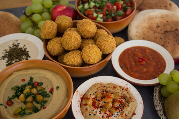 Traditional food of Israel on dark grey background with copy space. Colorful authentic meals top view photo: plate of hummus, falafels, salad, pita bread and tahini sauce. 
