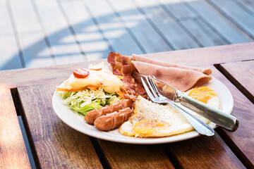 The English breakfast consists of fried eggs, bacon, sausage, and green salad.