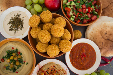   Authentic food of Middle East. Plate of hummus, falafels, pita bread, harissa sauce, tahini, fresh salad and fruits on wooden table. Traditional meals of Israel top view photo. Beautiful food pictur