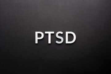 the word PTSD laid with silver metal letters on flat black background in directly above perspective