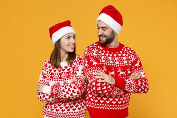 Pretty young Santa couple friends man woman in sweater Christmas hat holding hands crossed looking at each other isolated on yellow background studio. Happy New Year celebration merry holiday concept.