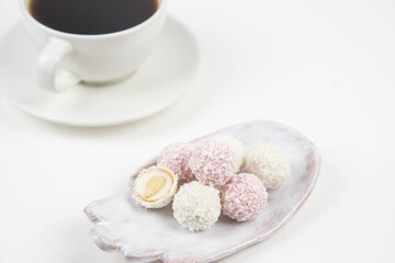 White coconut candy balls on handmade plate. Coconut cookies on white background with the cup of tea. Teapot with black tea. 