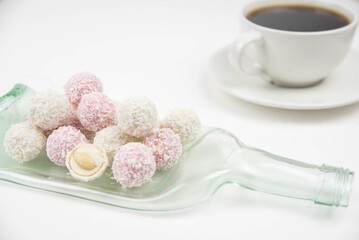 White coconut candy balls on handmade upcycle plate from the bottle. Coconut cookies on white background with the cup of tea. Teapot with black tea. 