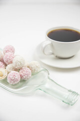 White coconut candy balls on handmade upcycle plate from the bottle. Coconut cookies on white background with the cup of tea. Teapot with black tea. 