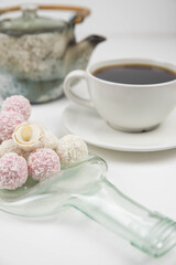 White coconut candy balls on handmade upcycle plate from the bottle. Coconut cookies on white background with the cup of tea. Teapot with black tea. 
