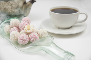 White coconut candy balls on handmade upcycle plate from the bottle. Coconut cookies on white background with the cup of tea. Teapot with black tea. 