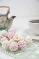 White coconut candy balls on handmade upcycle plate from the bottle. Coconut cookies on white background with the cup of tea. Teapot with black tea. 