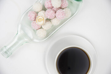 White coconut candy balls on handmade upcycle plate from the bottle. Coconut cookies on white background with the cup of tea. Teapot with black tea. 