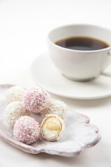Fototapeta na wymiar White coconut candy balls on handmade plate. Coconut cookies on white background with the cup of tea. Teapot with black tea. 