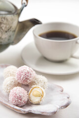 White coconut candy balls on handmade plate. Coconut cookies on white background with the cup of tea. Teapot with black tea. 