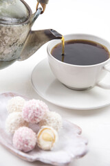 White coconut candy balls on handmade plate. Coconut cookies on white background with the cup of tea. Teapot with black tea. 