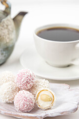 White coconut candy balls on handmade plate. Coconut cookies on white background with the cup of tea. Teapot with black tea. 