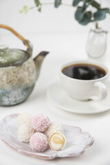 Obraz na płótnie Canvas White coconut candy balls on handmade plate. Coconut cookies on white background with the cup of tea. Teapot with black tea. 