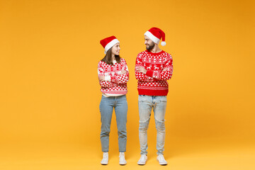 Full length of smiling young Santa couple friends man woman in sweater Christmas hat hold hands crossed looking at each other isolated on yellow background. Happy New Year celebration holiday concept.