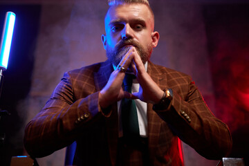self-confident brutal male in tuxedo is in contemplation indoors, elegant male sits on chair posing