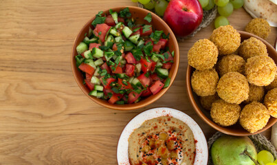   Authentic food of Middle East. Plate of hummus, falafels, pita bread, harissa sauce, tahini, fresh salad and fruits on wooden table. Traditional meals of Israel top view photo. Beautiful food pictur