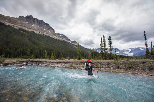 Backpacker crosses fast flowing river en route to Castleguard Meadows