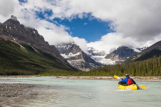 Explorer paddles yellow raft towards the Rocky Mountains, Banff.