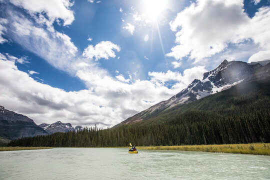 Distant view of person paddling kayak (packraft) in Rocky mountains.