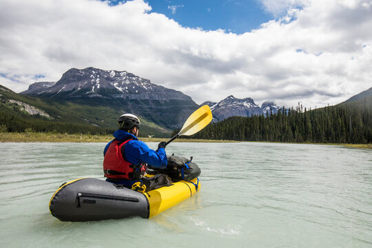 Man paddling yellow raft through vast valley in Banff National Park.
