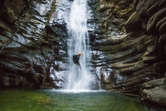 Man rappelling down waterfall approaches deep pool, Vancouver B.C.