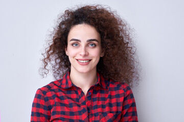 Portrait of armenian pretty curly haired brunette girl in plaid red shirt and positive smile on expressive face looking at camera isolated in studio